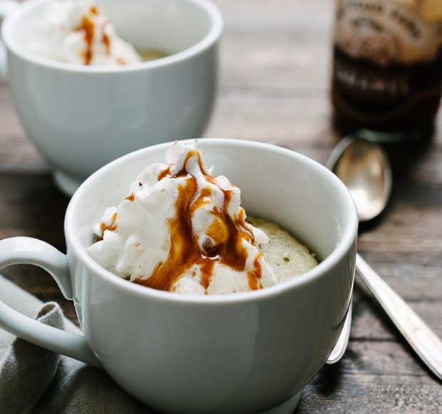 Two banana caramel mug cakes topped with whipped cream on a wooden surface.