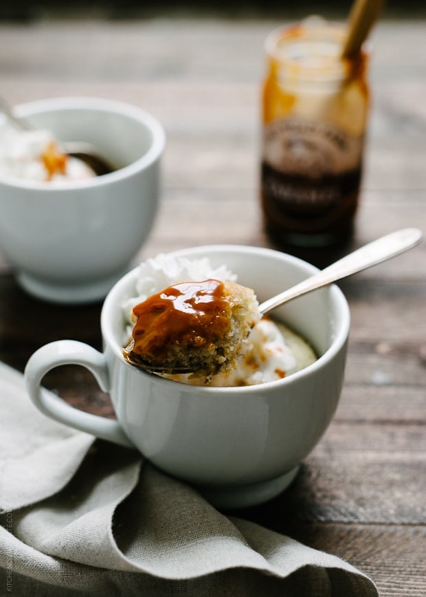 A microwave mug cake topped with caramel with a spoonful being removed.