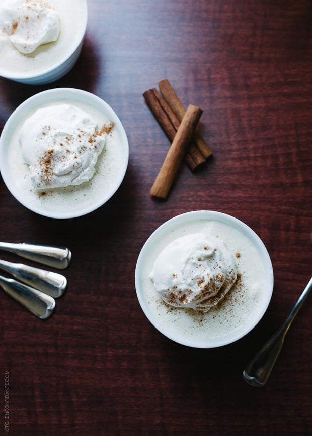 Cinnamon sticks, spoons, and cups of eggnog mousse on a wooden background.