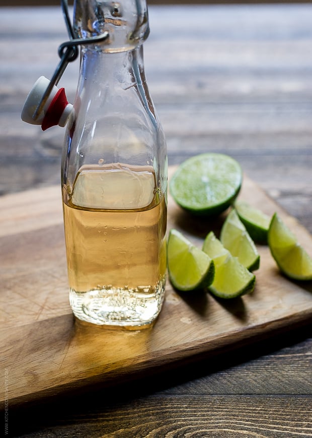 A glass bottle of ginger beer and slices of lime on a wooden surface.