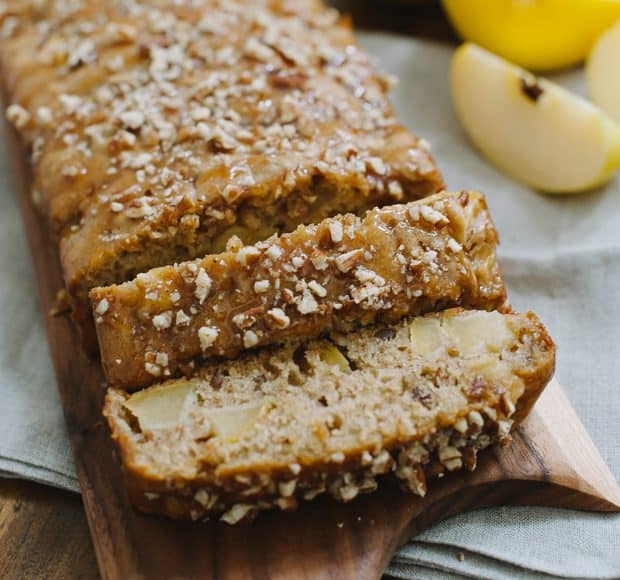 Slices of an apple pecan loaf cake on a wooden surface.