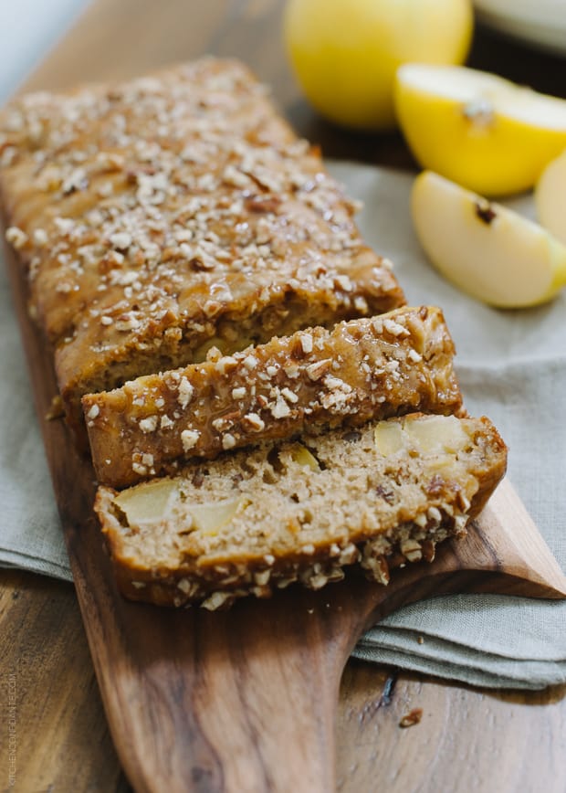 Slices of an apple pecan loaf cake on a wooden surface.