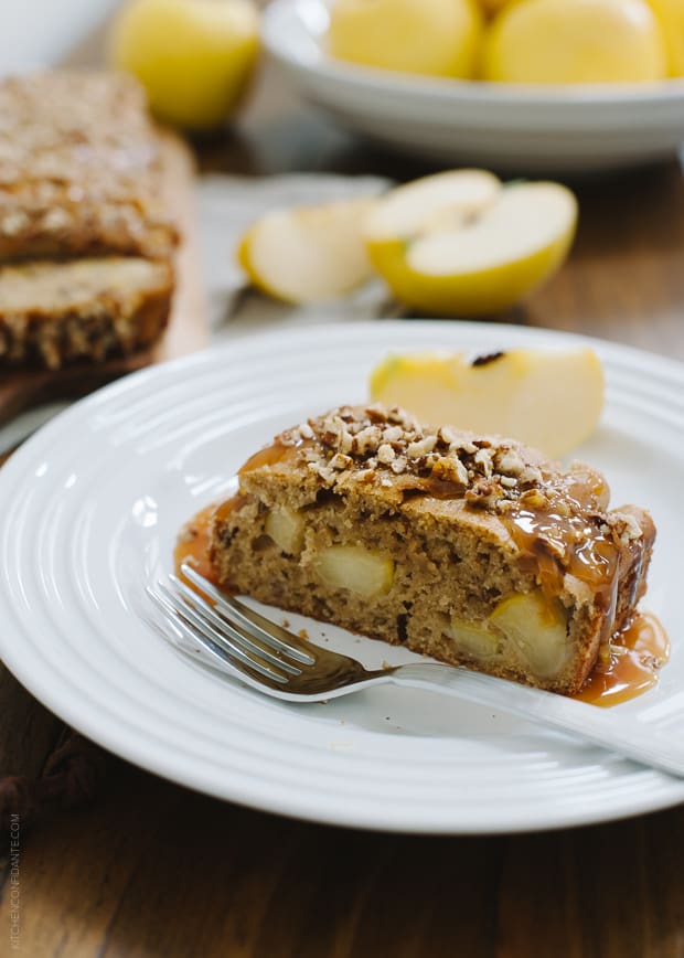 A slice of apple pecan loaf cake topped with chopped pecans and caramel sauce.