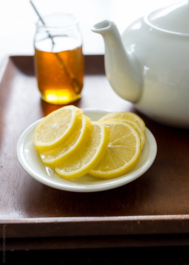 Lemon slices on a white plate with a teapot in the background.