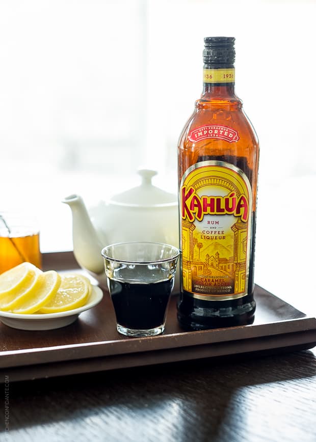 Kahlúa bottle on a tray with lemon slices and a teapot in the background.