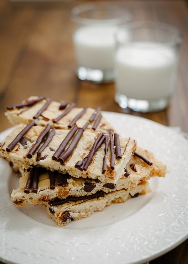 Chocolate Butterscotch Cookie Brittle stacked on a white plate with glasses of milk in the background.