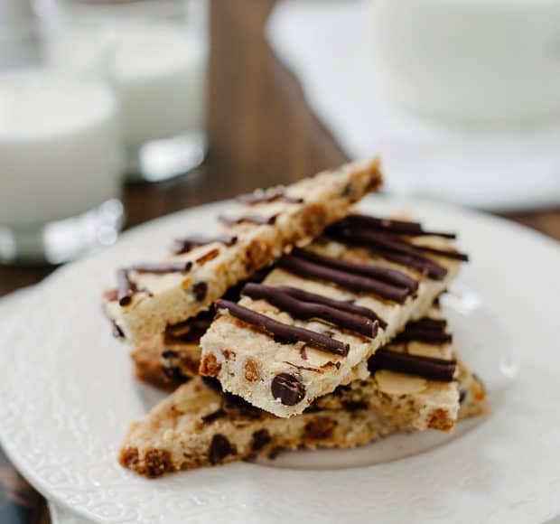 Chocolate Butterscotch Cookie Brittle stacked on a white plate with glasses of milk in the background.