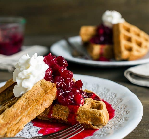 Gingerbread Belgian Waffles served on a white plate with cranberry compote and a whipped cream topping.