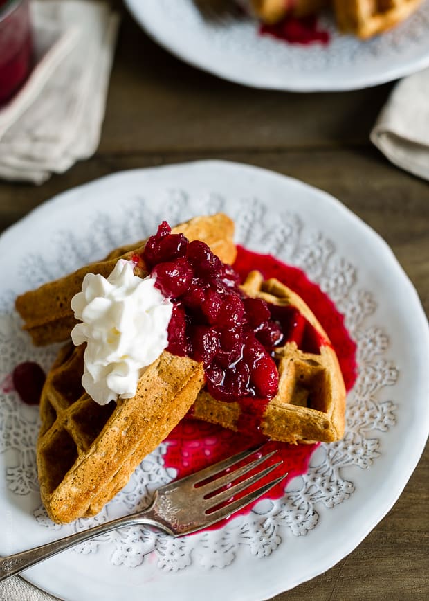 Waffles served on a white plate with cranberry compote and a whipped cream topping.