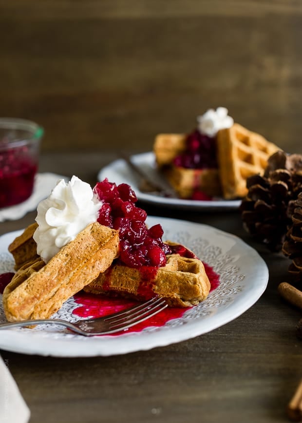Gingerbread Belgian Waffles served on a white plate with cranberry compote and a whipped cream topping.