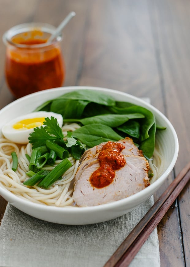 A bowl of Harissa Ramen topped with pork slices, a soft egg, spinach and harissa.