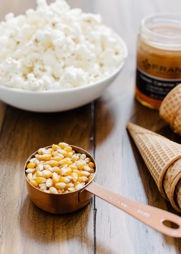 A scoop of popcorn kernels with popcorn in the background.