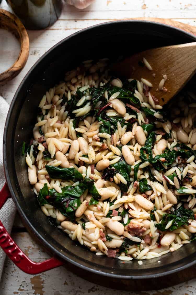 Swiss Chard with Orzo, Cannellini Beans and Pancetta in a red Staub Dutch oven.