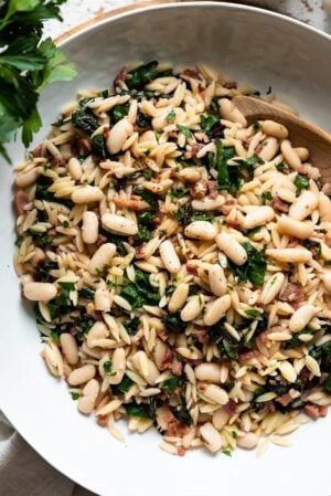Swiss Chard with Orzo, Cannellini Beans and Pancetta in a white serving dish.