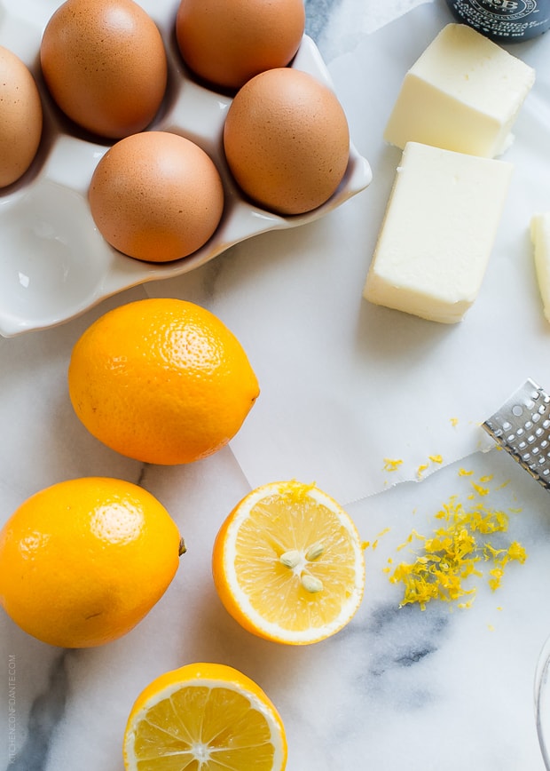 Meyer lemons on a marble surface surrounded by zest, eggs, and butter.