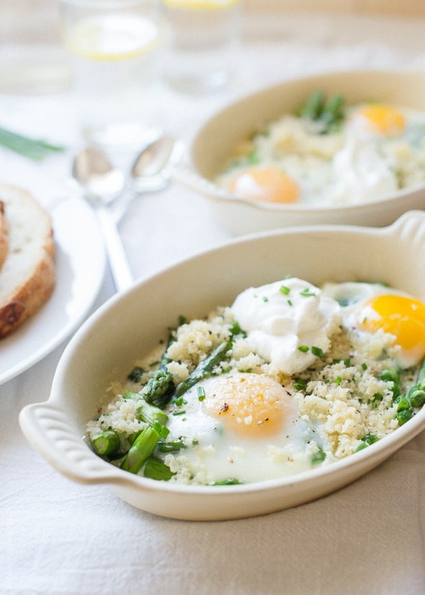 A small white ramekin filled with baked eggs, asparagus, and peas.