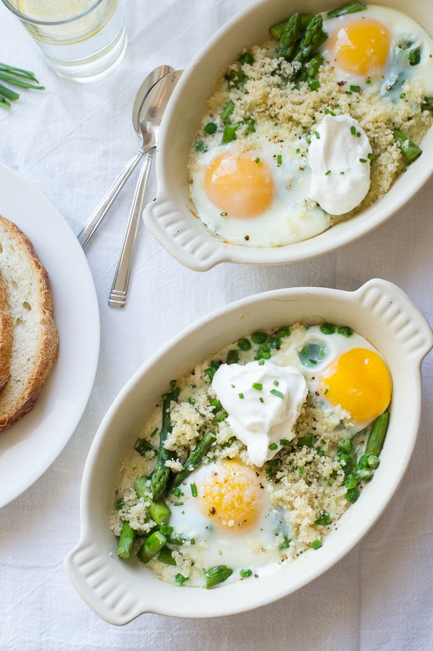 Small white ramekins filled with baked eggs, asparagus, and peas.