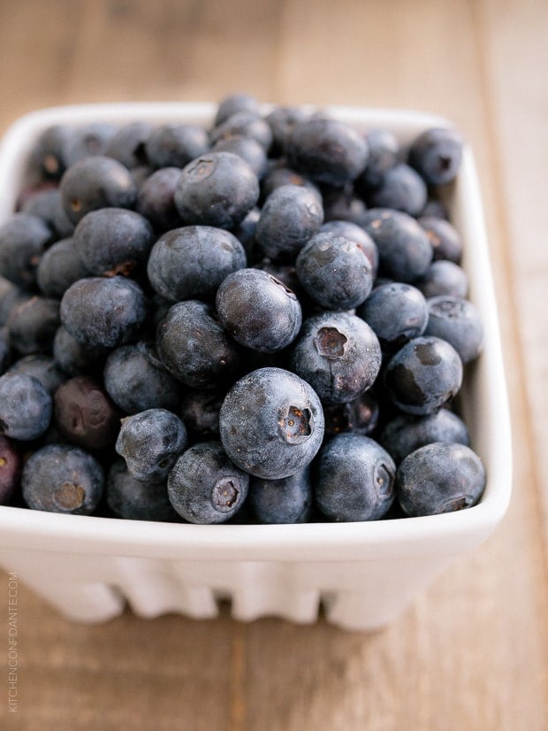 Fresh blueberries in a white container on a wooden surface.