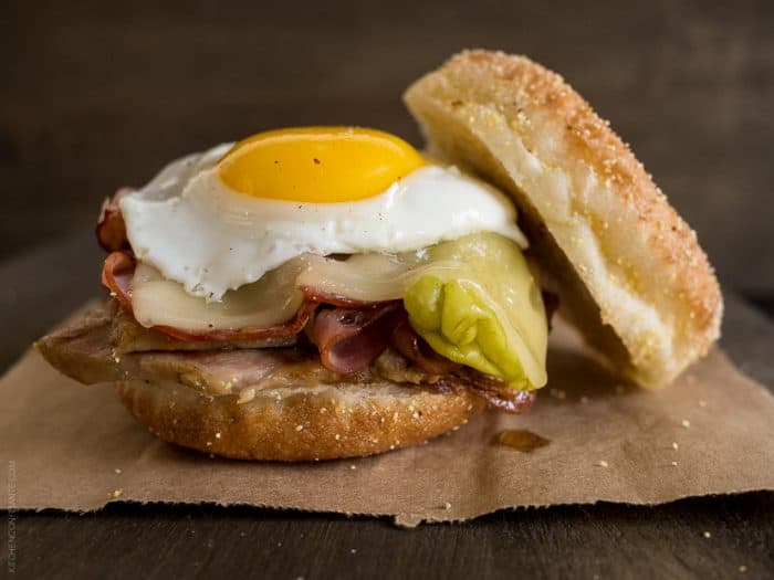 A Cubano Breakfast Sandwich made with an English Muffin and piled high with meat and a sunny side up egg.