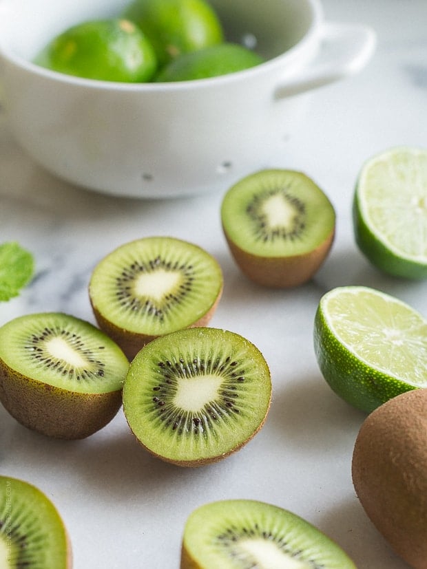 Fresh kiwis and limes cut in half on a white surface.