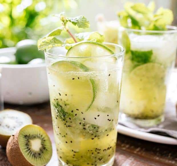 Kiwi Lime Mojitos surrounded by fresh kiwi on a wooden surface.