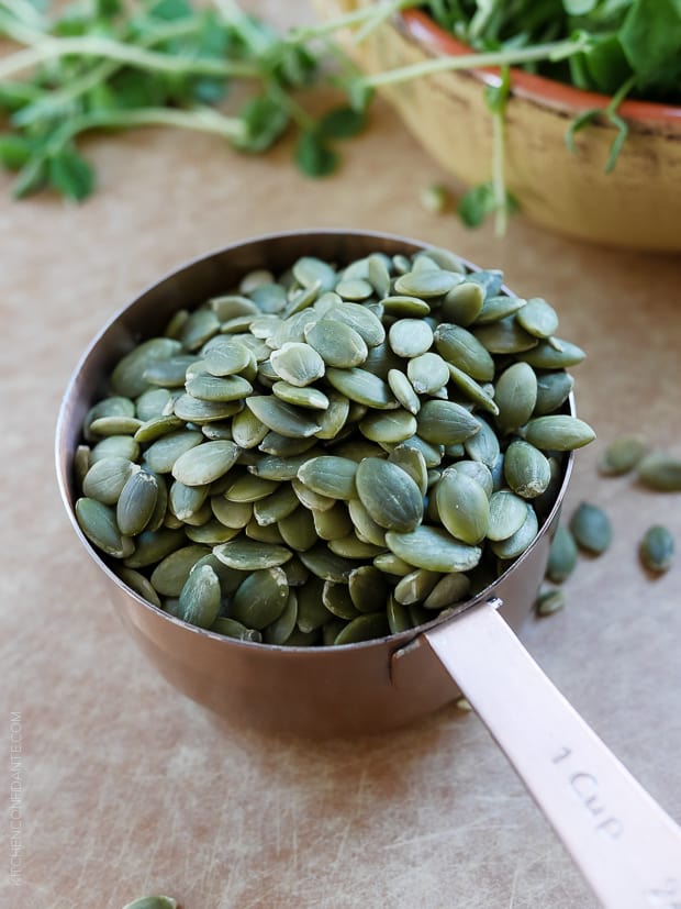 A measuring cup filled with pumpkin seeds.