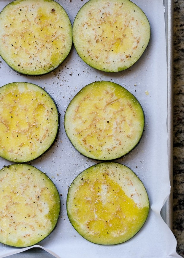 Slices of eggplant on a sheet pan, ready to roast in the oven.