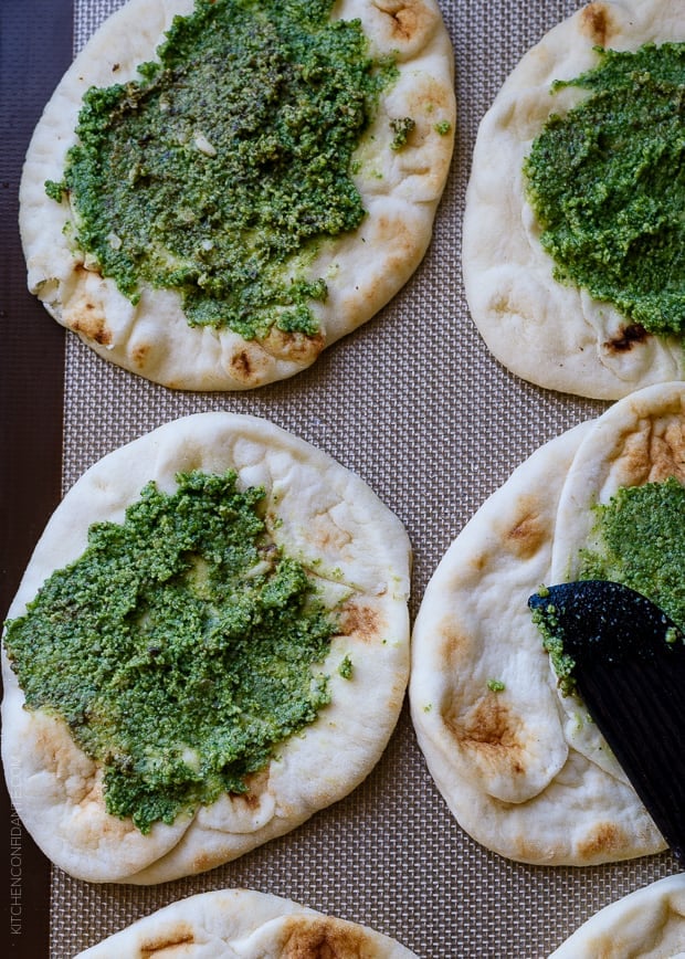 Mini naan spread with pesto on a baking sheet.