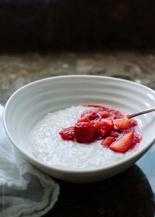 A white bowl of Coconut Tapioca Pudding with a spoonful of bright red Strawberry Rhubarb Compote on top.