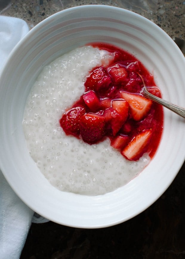 A white bowl of Coconut Tapioca Pudding with a spoonful of bright red Strawberry Rhubarb Compote on top.