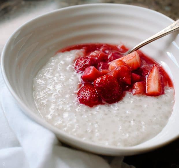 A white bowl of Coconut Tapioca Pudding with a spoonful of bright red Strawberry Rhubarb Compote on top.