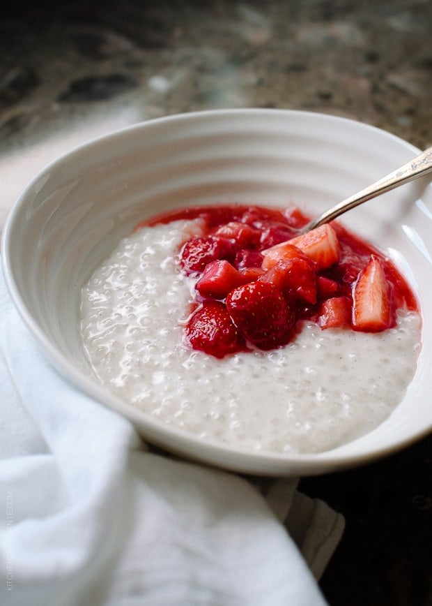 A white bowl of Coconut Tapioca Pudding with a spoonful of bright red Strawberry Rhubarb Compote on top.