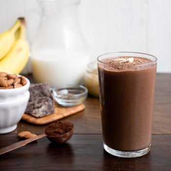 A Dark Chocolate Almond Butter Smoothie in a glass on a wooden surface.