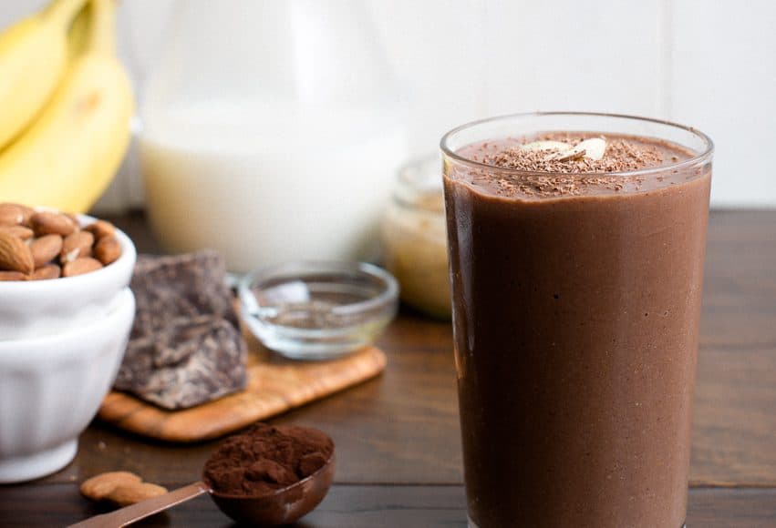 A Dark Chocolate Almond Butter Smoothie in a glass on a wooden surface.