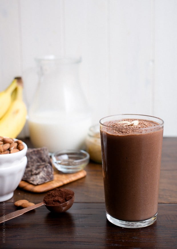 A Dark Chocolate Almond Butter Smoothie in a glass on a wooden surface.