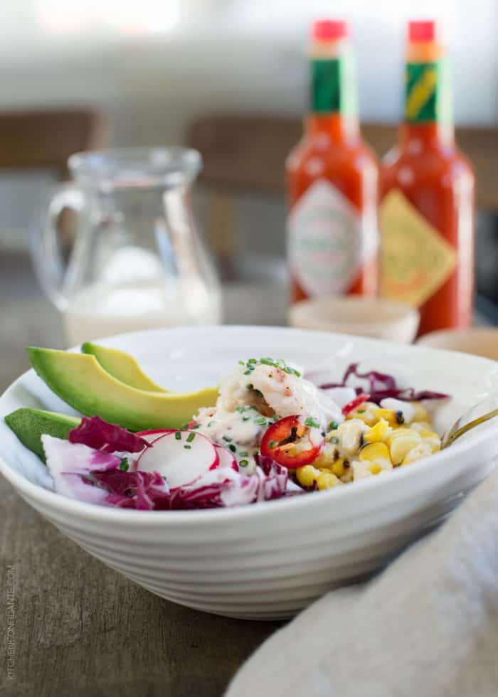 Dungeness Crab Salad in a white bowl garnished with red cabbage, radishes, and sliced avocado.