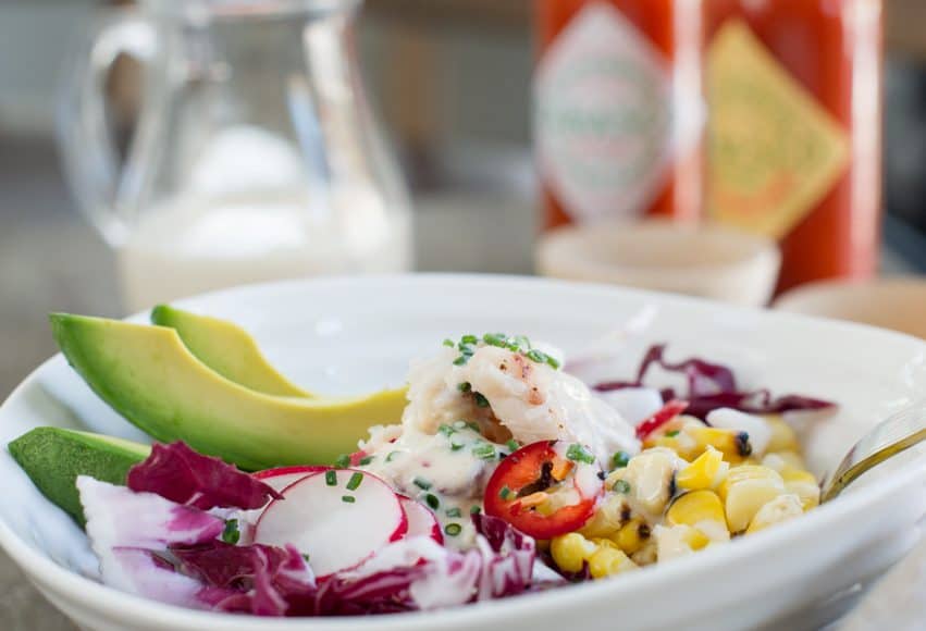 Dungeness Crab Salad in a white bowl garnished with red cabbage, radishes, and sliced avocado.