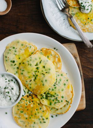 Pancakes made with fresh peas on a white plate with a side dish of homemade tzatziki.