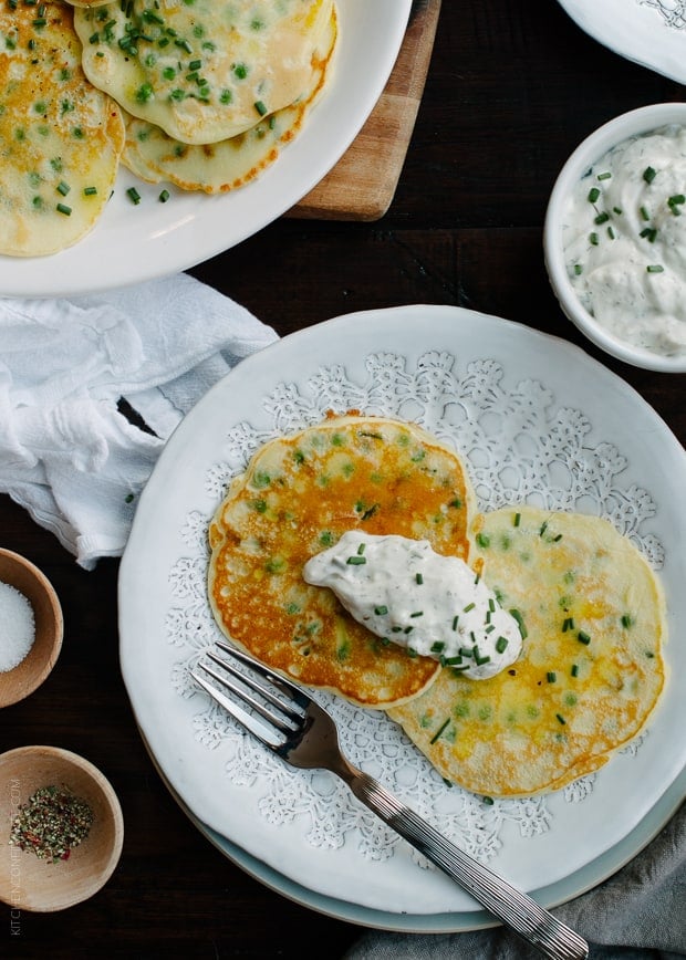 Two pea pancakes on a white plate with a side dish of homemade tzatziki.
