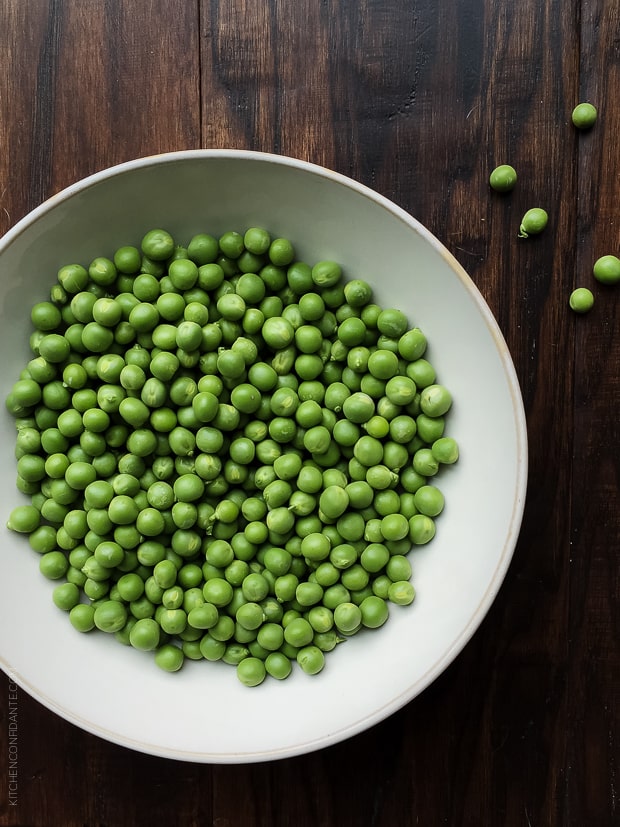 A white bowl filled with fresh green peas.