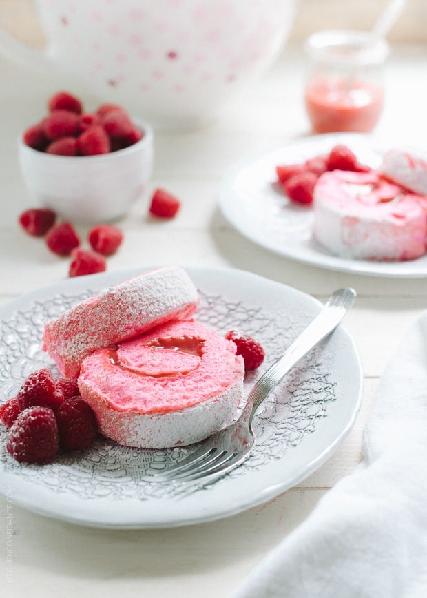 Pink slices of a Raspberry Meringue Roll on a white plate garnished with fresh raspberries.