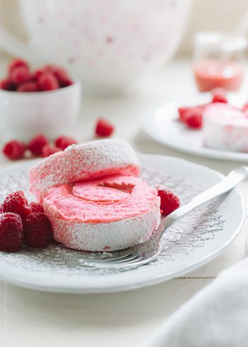 Pink slices of a Raspberry Meringue Roll on a white plate garnished with fresh raspberries.