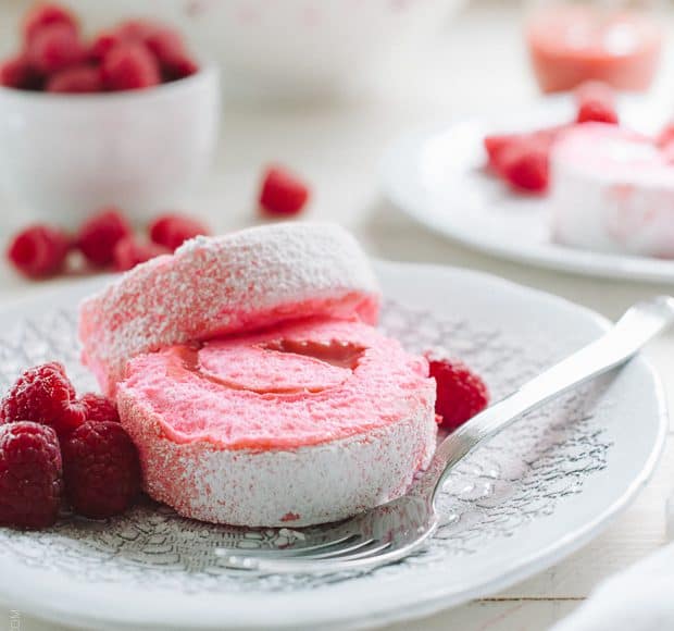 Pink slices of a Raspberry Meringue Roll on a white plate garnished with fresh raspberries.