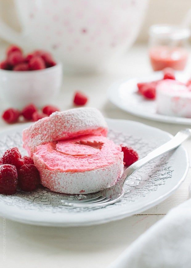 Pink slices of a Raspberry Meringue Roll on a white plate garnished with fresh raspberries.