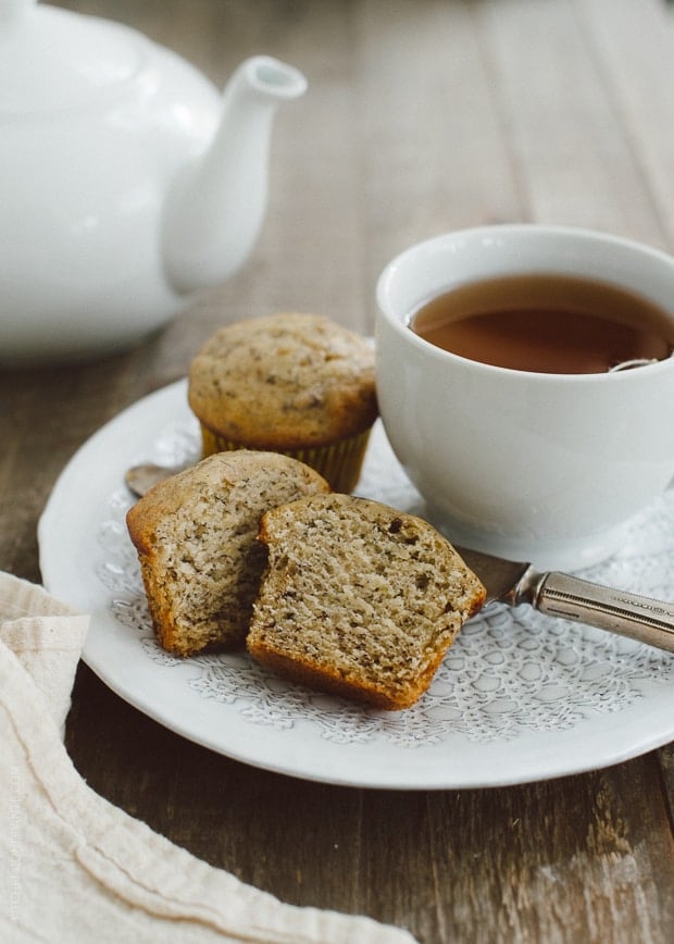 A Banana Nut Ricotta Muffin halved on a plate alongside a cup of tea. 