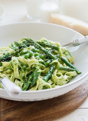 A bowl filled with Fettuccine topped with Creamy Spinach Sauce, Asparagus and Peas.
