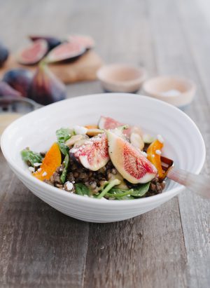 Fig and Apricot Summer Lentil Salad in a white bowl on a wooden surface.