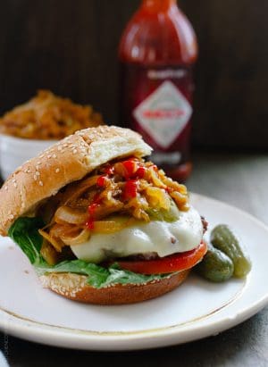 A hamburger loaded with toppings like cheese, tomato, pickles, and Sriracha Caramelized Onions.