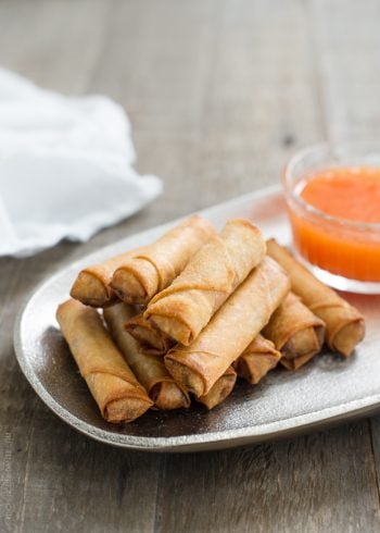 Lumpiang Shanghai - Filipino Spring Rolls (Lumpia) stacked on a platter with dipping sauce in the background