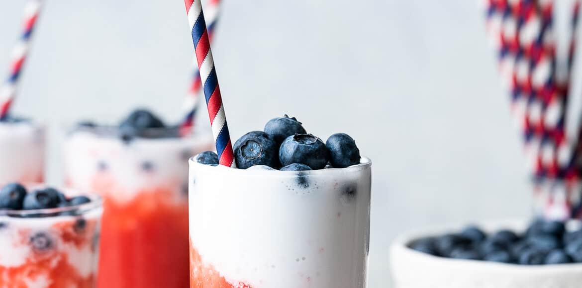 Slushies in tall glasses layered red and white and topped with fresh blueberries.